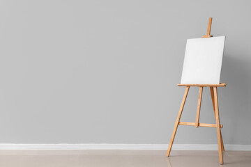 Wooden easel with blank canvas near grey wall