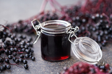 Homemade black elder syrup in a glass jar with fresh elderberries