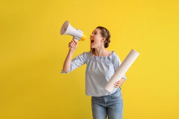 Fotobehang Young woman with paper roll shouting into megaphone on yellow background © Pixel-Shot