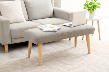 Laptop with newspapers on soft bench in living room