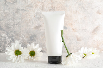 Tube of cosmetic product and chamomile flowers on grunge background