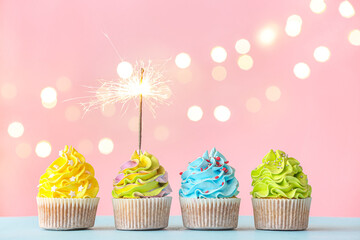 Tasty birthday cupcakes with sparkler on color background