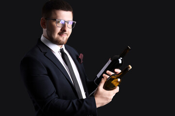 Young sommelier holding bottles with different types of wine on black background