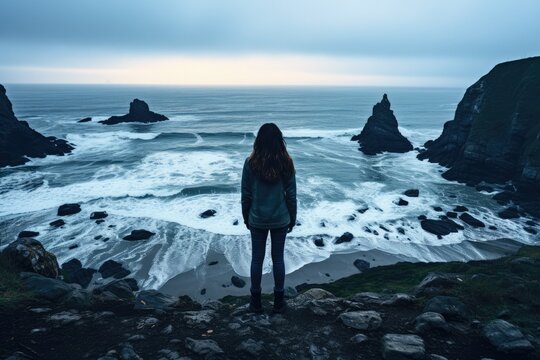 Woman standing in front of the ocean and looking at the stormy sea - Generative AI