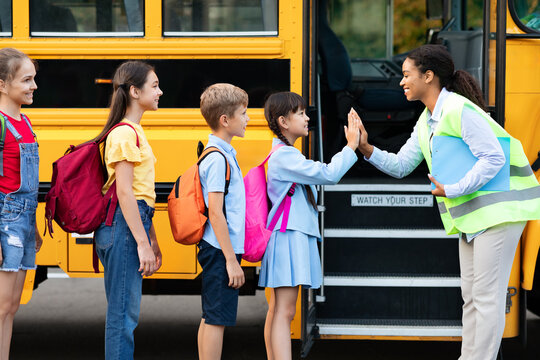 Kids boarding school bus receiving joyful high five from smiling black teacher