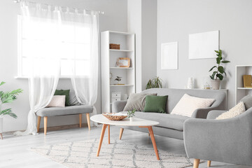 Interior of light living room with grey sofa, table and armchair