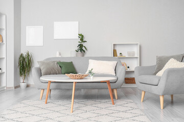 Interior of light living room with grey sofa, table and armchair