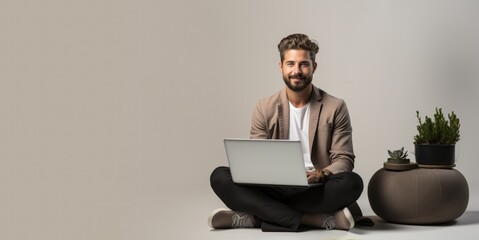 A young handsome guy with a laptop sits cross-legged