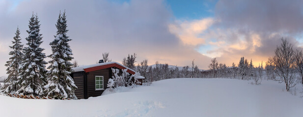 A small snow covered hunting lodge in the norwegian mountains with animal traces in the foreground...