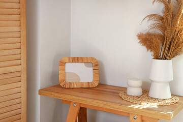 Vase with pampas grass and frame on table in room
