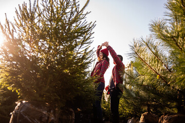 Couple in love in checkered red shirts knitted hats dances, spins among green Christmas tree market