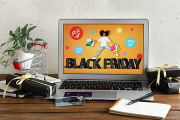 Laptop with Black Friday sale advertisement, credit cards and gift boxes on wooden table
