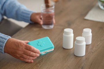 Senior woman with pill box and glass of water in kitchen, closeup
