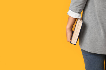 Beautiful young Asian woman with Bible on yellow background, back view