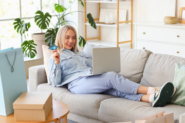 Young woman with laptop, credit card and bags shopping online at home