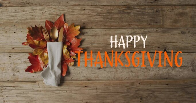 Animation of happy thanksgiving text over cutlery and autumn leaves over wooden surface