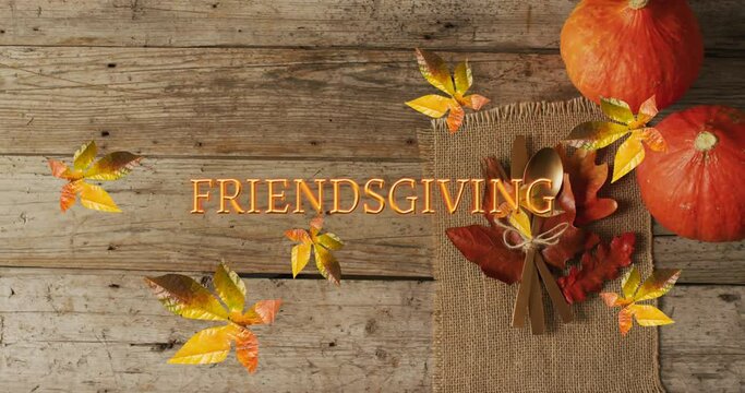 Animation of friendsgiving text over cutlery and autumn leaves over wooden surface