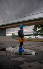 A lonely little boy standing in a puddle on a rainy day