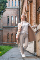 Young slender woman in white clothes near old red brick building looking into the side. Girl alone. Vertical frame.