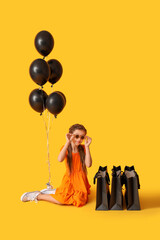Little girl with balloons and shopping bags sitting on yellow background