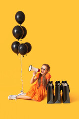 Little girl with megaphone, shopping bags and balloons sitting on yellow background