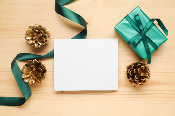 Beautiful Christmas composition with blank card, gift box and pine cones on wooden background