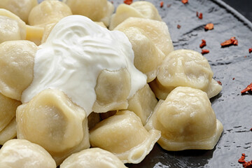 Dumplings with sour cream and microgreen, on a black glossy plate