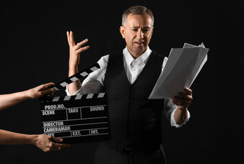 Mature actor reading script and hands with clapperboard on dark background