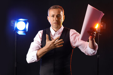 Mature actor reading film script on dark background