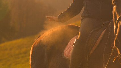 CLOSE UP: A rider in the saddle pats a horse from which a cloud of dust rises