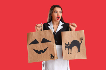 Shocked young woman dressed for Halloween as maid with gift bags on red background