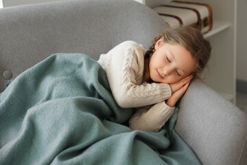 Cute little girl with warm plaid lying in armchair at home