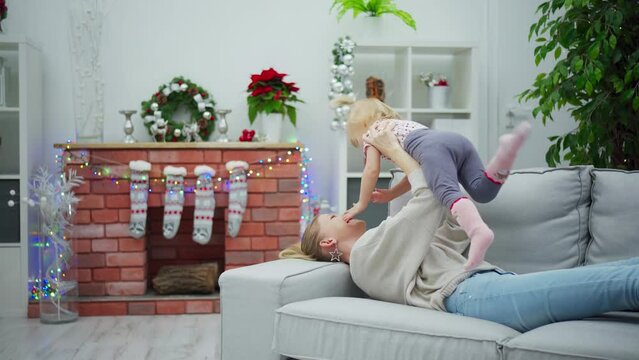 During the holidays, a mother plays with her little daughter while lying on the couch.
