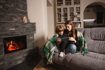 Happy mother and child are playing with a toy train near the fireplace. Mother and child sitting...