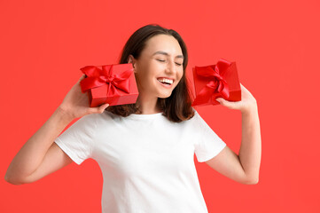 Beautiful young woman in pajamas with gift boxes on red background