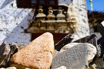 Mani stones with Tibetan mantras on a Tibetan-style house door in Nako village, Spiti Valley, India, with blurred stupas in the background.