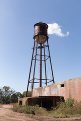 A beautiful water tower is set around an abandoned area. This rusty metal structure stands tall against a blue sky.