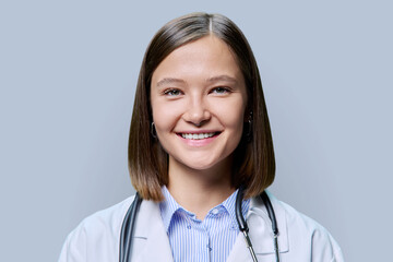 Headshot portrait of young friendly female medical worker on gray background