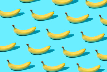 Trendy Summer food pattern made with yellow bananas on bright light blue background. Minimal summer concept.