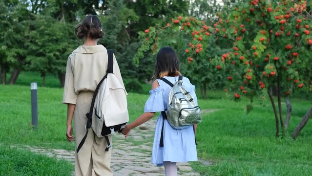 Two girls walking in the park in the summer, talking, walking after school and college, holding hands, best friends, sisters returning home after school