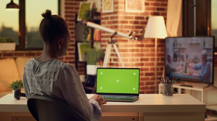 Teleworker using greenscreen on laptop while working remotely on freelance job, looking at copyspace template on device screen. African american woman works with isolated chroma key.