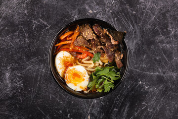 Rice bowl with beef, noodles, egg and vegetables on a dark background