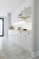 Kitchen with white cabinets, warm lighting and large metal hood.