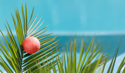 Christmas ball on palm tree branch on background of blue water pool at summer resort. Happy New...