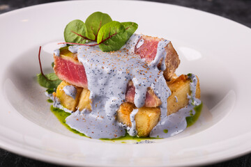 grilled tuna with greens on a white plate on a dark background