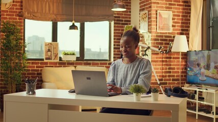 Home based african american developer begins day by solving assignments for online networking job. Woman freelancer using laptop at workstation to reply to emails, natural light at sunset.