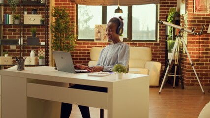 Relaxed woman listens to music, typing information on laptop at workstation. African american teleworker creating online career, enjoying remote job at home office while singing songs.