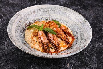 Shrimp with basil on a plate on a dark stone background.