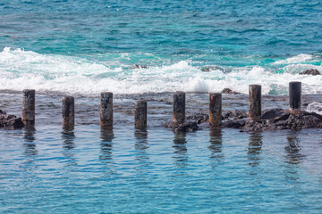 Wooden pillars breakwaters in the ocean . Water's edge with waves