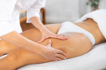 Female masseuse doing thigh massage closeup to young woman client